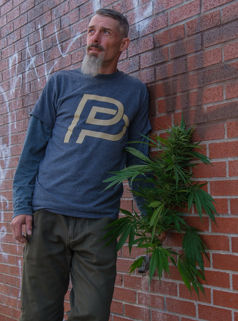 OG male wearing a blue t-shirt with gold prohibition prophets logo.