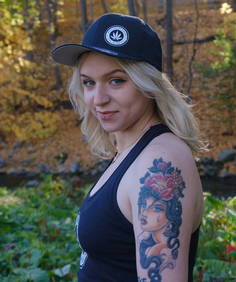 Female wearing black prohibition prophets tank top and black prohibition prophets hat with pot leaf logo design. 